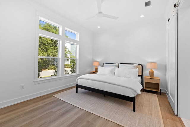 bedroom with a barn door, multiple windows, ceiling fan, and light hardwood / wood-style floors