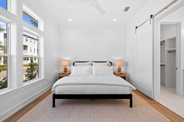 bedroom featuring a barn door, ceiling fan, crown molding, and light hardwood / wood-style flooring