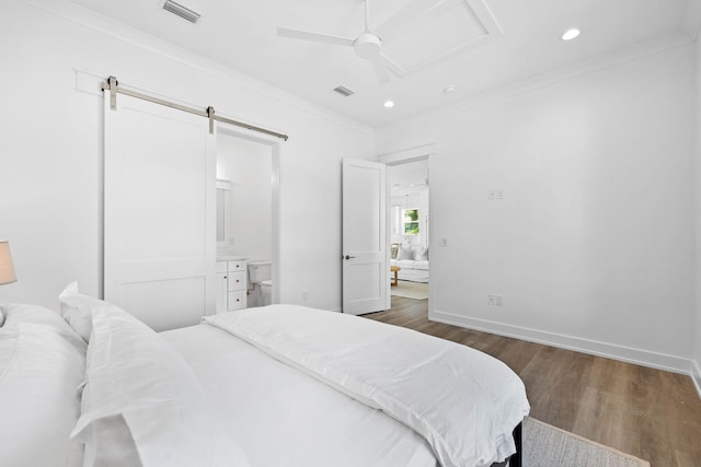 bedroom featuring a barn door, dark wood-type flooring, ceiling fan, connected bathroom, and ornamental molding