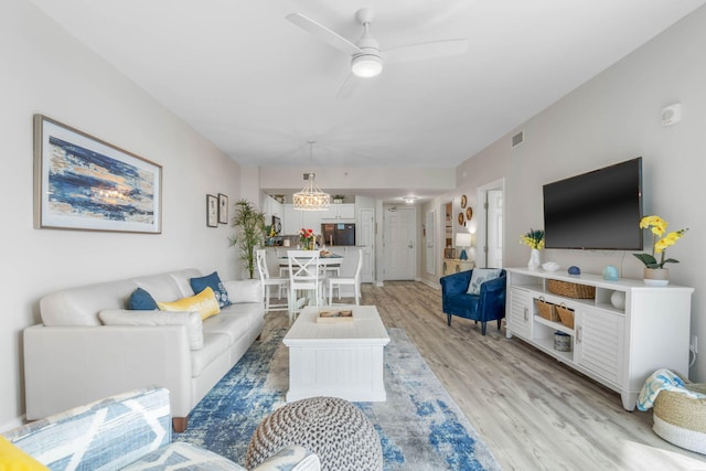 living room with ceiling fan with notable chandelier and light hardwood / wood-style flooring