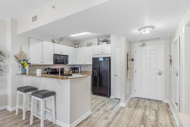 kitchen featuring light wood-type flooring, black appliances, kitchen peninsula, light stone countertops, and white cabinets