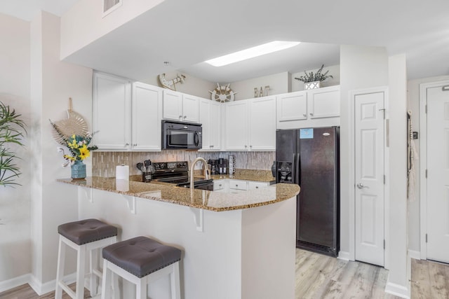 kitchen with black appliances, light stone countertops, tasteful backsplash, and kitchen peninsula