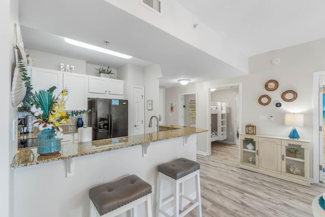 kitchen featuring white cabinets, light stone counters, light hardwood / wood-style floors, black refrigerator with ice dispenser, and a breakfast bar area