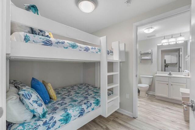 bedroom with connected bathroom, light hardwood / wood-style floors, and sink