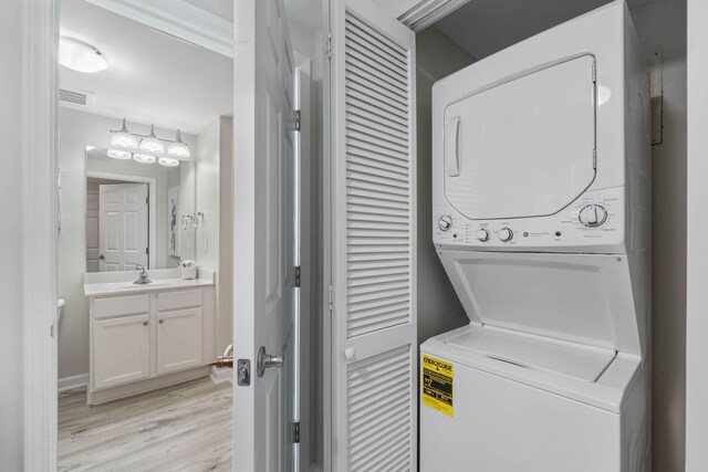 washroom featuring stacked washer / dryer, light hardwood / wood-style flooring, and sink