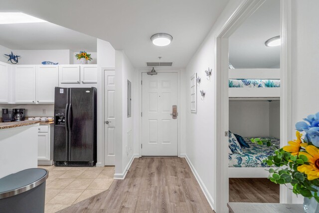 interior space with electric panel, light wood-type flooring, black fridge with ice dispenser, and white cabinets