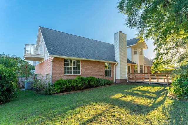 back of property with brick siding, a yard, a chimney, roof with shingles, and a balcony