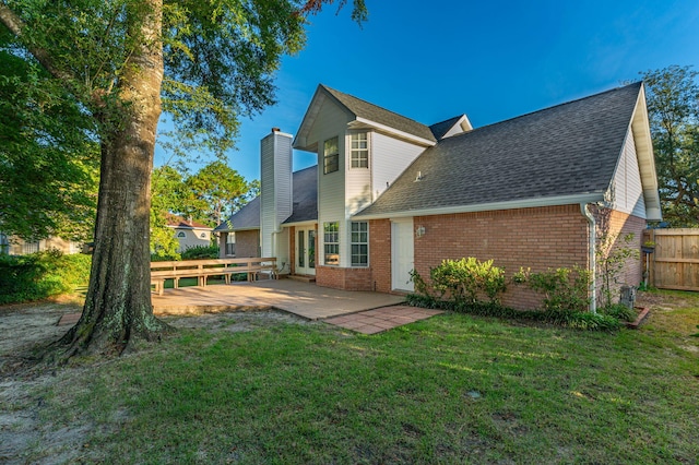 rear view of house with brick siding, a chimney, a lawn, a patio area, and fence