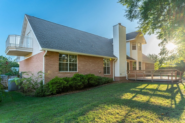 rear view of house featuring a balcony, brick siding, a yard, roof with shingles, and a chimney