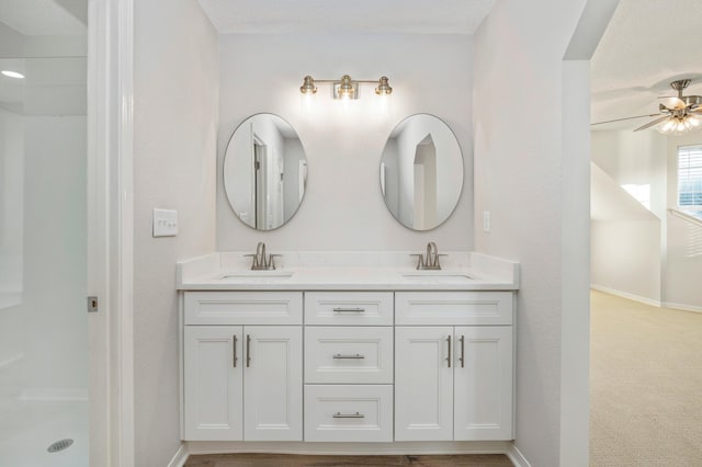 bathroom featuring double vanity, walk in shower, a sink, and baseboards