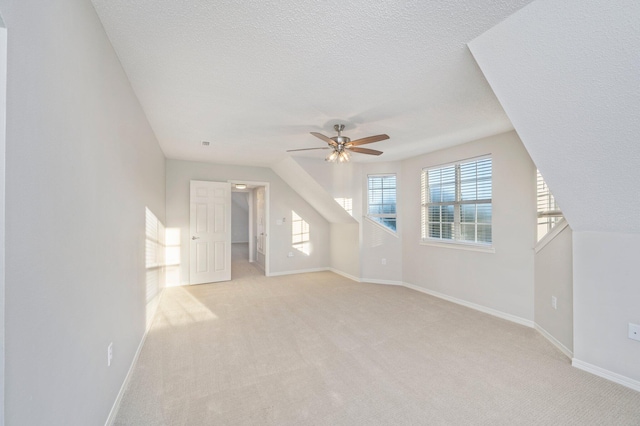 additional living space with a ceiling fan, light carpet, a textured ceiling, and baseboards