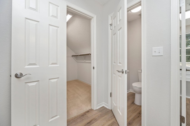 bathroom featuring a walk in closet, baseboards, toilet, and wood finished floors