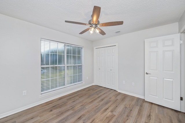 unfurnished bedroom with a closet, wood finished floors, visible vents, and baseboards