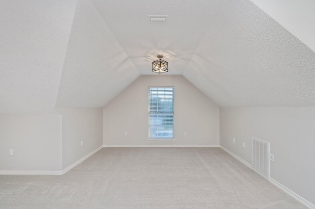 additional living space featuring visible vents, vaulted ceiling, a textured ceiling, and light colored carpet