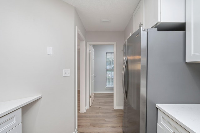 kitchen with baseboards, white cabinets, freestanding refrigerator, a textured ceiling, and light wood-style floors