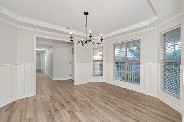 unfurnished dining area with light wood-style floors, a tray ceiling, and wainscoting