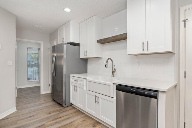 kitchen with a sink, white cabinetry, light countertops, appliances with stainless steel finishes, and backsplash