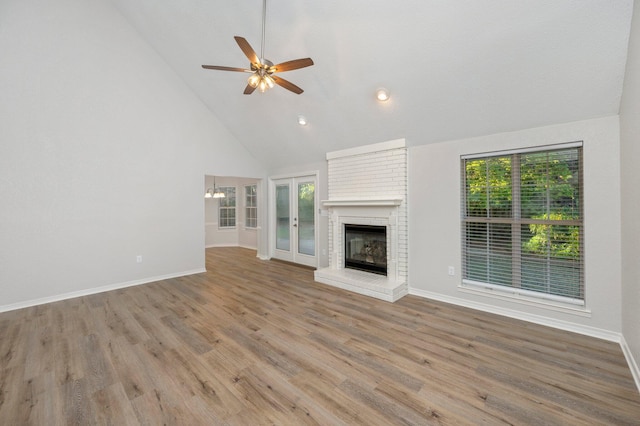 unfurnished living room featuring high vaulted ceiling, ceiling fan with notable chandelier, a fireplace, wood finished floors, and baseboards