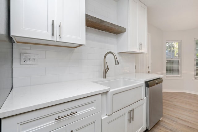 kitchen with light wood finished floors, stainless steel dishwasher, a sink, and white cabinetry