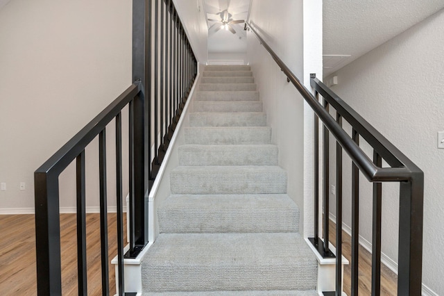 stairway featuring baseboards, wood finished floors, and a textured wall