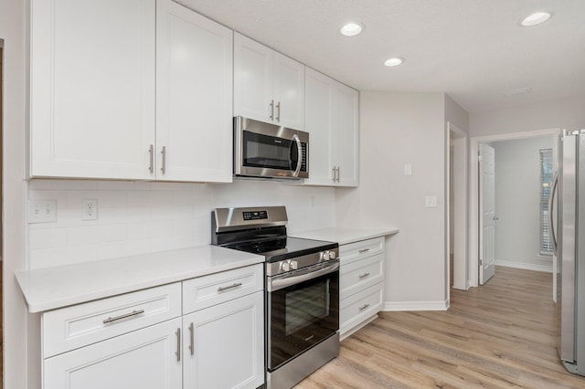 kitchen featuring white cabinetry, light countertops, appliances with stainless steel finishes, light wood-type flooring, and decorative backsplash