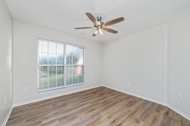 empty room featuring a textured ceiling, wood finished floors, visible vents, a ceiling fan, and baseboards