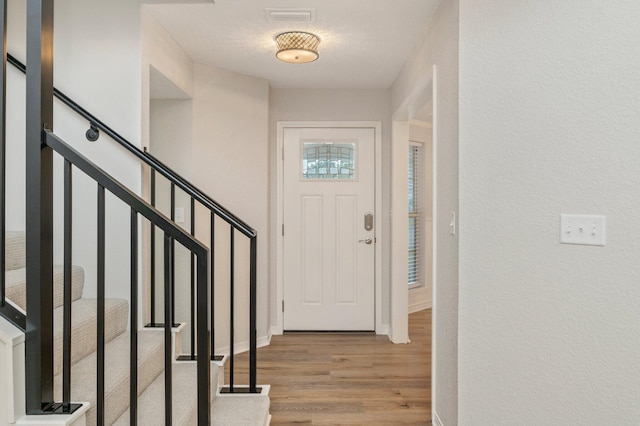 entryway with stairway, wood finished floors, visible vents, and baseboards