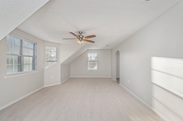 additional living space featuring arched walkways, light colored carpet, a ceiling fan, a textured ceiling, and baseboards