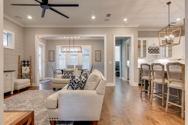 living room with ceiling fan with notable chandelier, hardwood / wood-style flooring, and crown molding