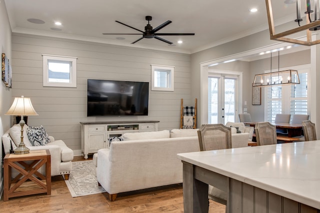 living room featuring wooden walls, light hardwood / wood-style flooring, ceiling fan with notable chandelier, and french doors