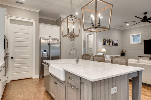 kitchen with light stone counters, stainless steel appliances, pendant lighting, white cabinetry, and an island with sink