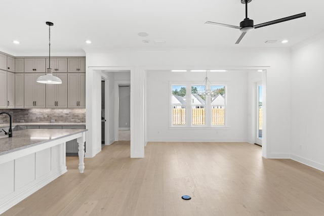 kitchen with gray cabinetry, ceiling fan with notable chandelier, light wood-type flooring, ornamental molding, and tasteful backsplash