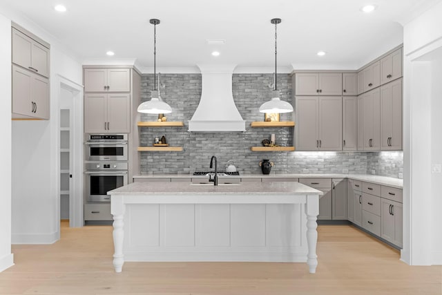 kitchen featuring gray cabinetry, stainless steel double oven, light hardwood / wood-style flooring, backsplash, and a kitchen island with sink