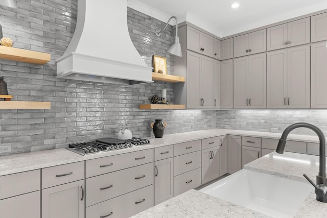 kitchen featuring sink, light stone counters, backsplash, stainless steel gas stovetop, and custom range hood