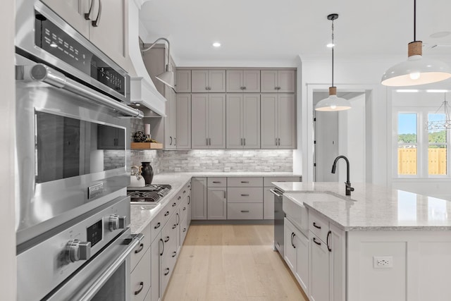 kitchen with light stone countertops, appliances with stainless steel finishes, tasteful backsplash, a center island with sink, and hanging light fixtures