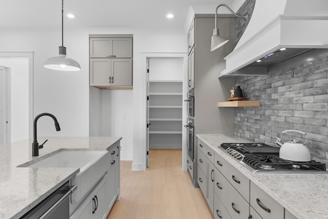 kitchen with light stone counters, premium range hood, hanging light fixtures, and stainless steel appliances