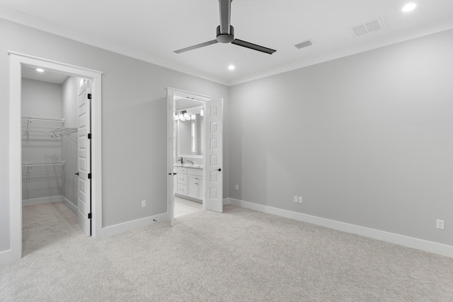 unfurnished bedroom featuring ensuite bath, a spacious closet, ceiling fan, light carpet, and a closet