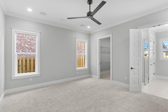 unfurnished bedroom with ceiling fan, crown molding, a spacious closet, and light carpet