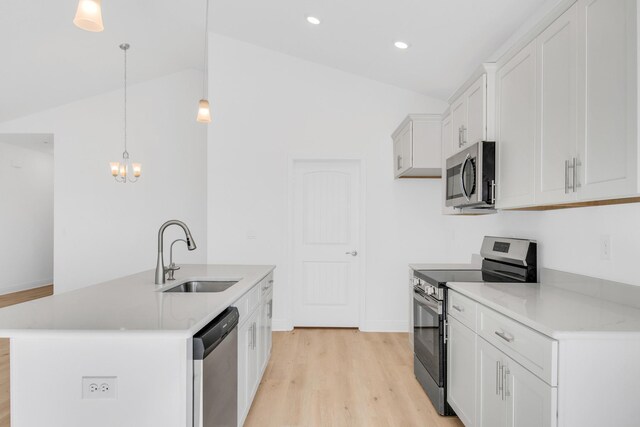 kitchen with vaulted ceiling, decorative light fixtures, stainless steel appliances, sink, and a kitchen island with sink