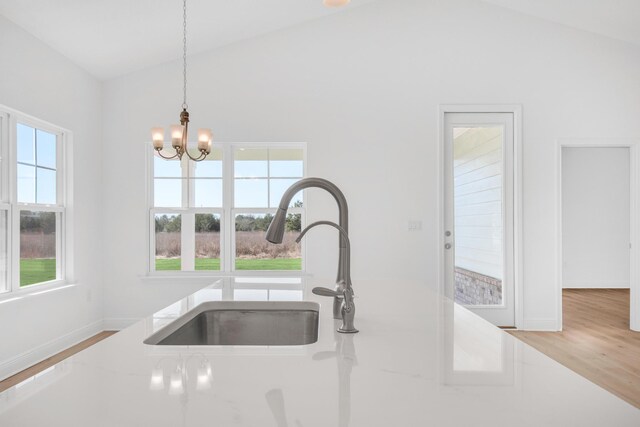 kitchen with an inviting chandelier, light hardwood / wood-style flooring, pendant lighting, sink, and high vaulted ceiling