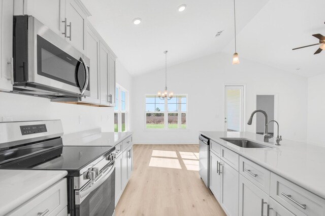 kitchen featuring ceiling fan with notable chandelier, stainless steel appliances, sink, lofted ceiling, and light hardwood / wood-style floors