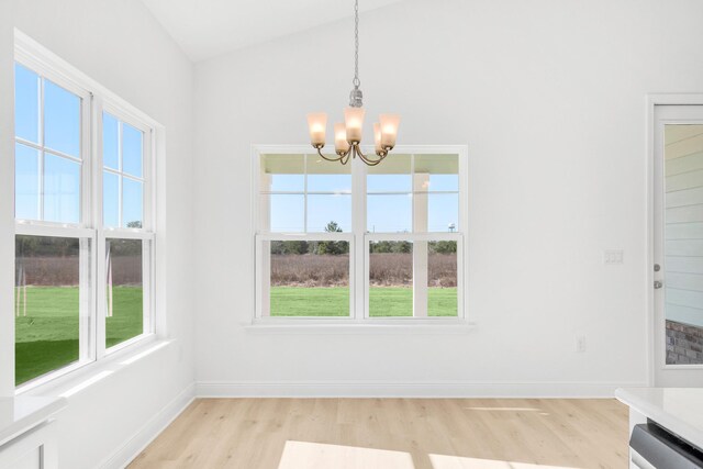 unfurnished dining area with vaulted ceiling, an inviting chandelier, and light wood-type flooring