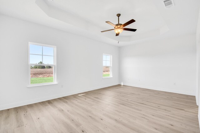 unfurnished room featuring a tray ceiling, ceiling fan, a wealth of natural light, and light hardwood / wood-style floors