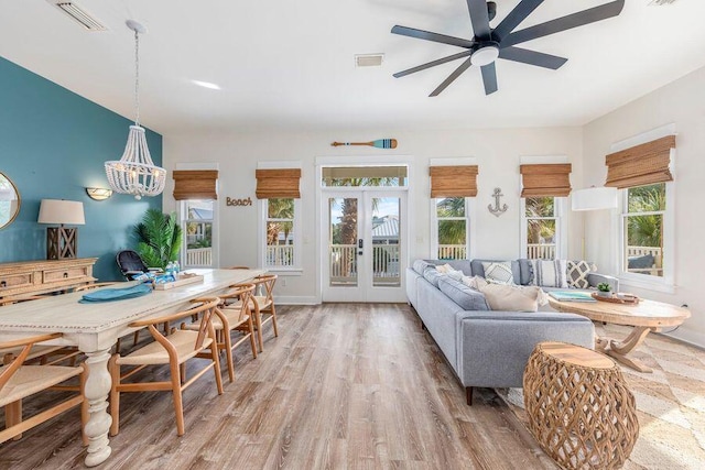 living room with light wood-type flooring, ceiling fan with notable chandelier, and french doors