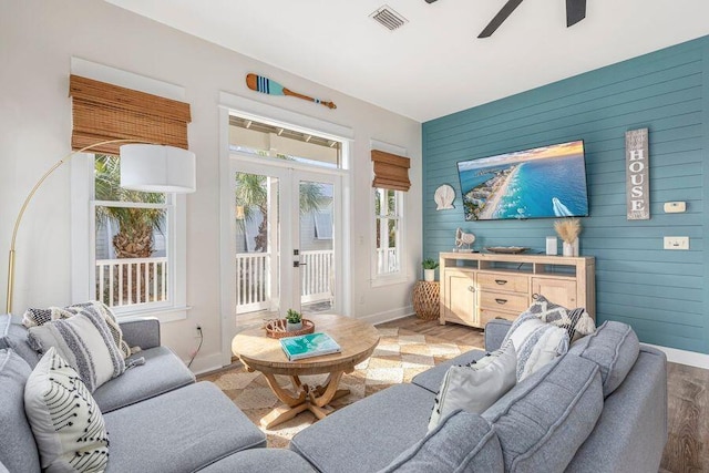 living room with ceiling fan, wood walls, hardwood / wood-style floors, and french doors