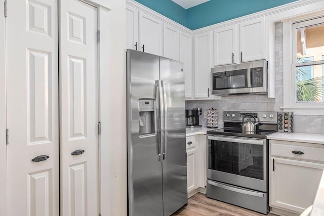 kitchen with appliances with stainless steel finishes, white cabinetry, light hardwood / wood-style flooring, and decorative backsplash