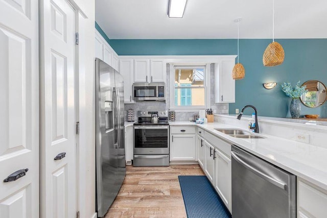 kitchen featuring white cabinets, hanging light fixtures, stainless steel appliances, light hardwood / wood-style floors, and sink