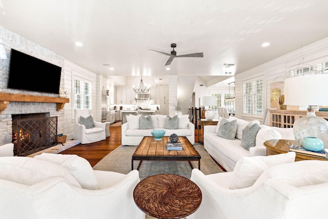 living room featuring ceiling fan with notable chandelier, a stone fireplace, and hardwood / wood-style floors