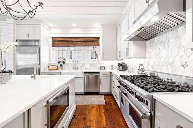 kitchen featuring sink, backsplash, range hood, built in appliances, and white cabinets