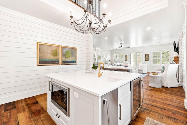 kitchen featuring dark hardwood / wood-style floors, black microwave, white cabinets, hanging light fixtures, and a kitchen island with sink